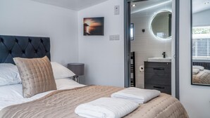 Un letto rifatto con cura, coperta beige, poggiatesta scuro e una foto appesa al muro raffigurante un tramonto.