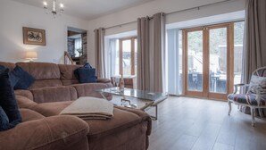 A spacious living room with a brown sofa, a glass coffee table, and a view of the outdoors through large sliding glass doors.