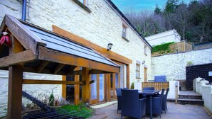 A stone building with a wooden pergola, outdoor seating, and a barbecue area.