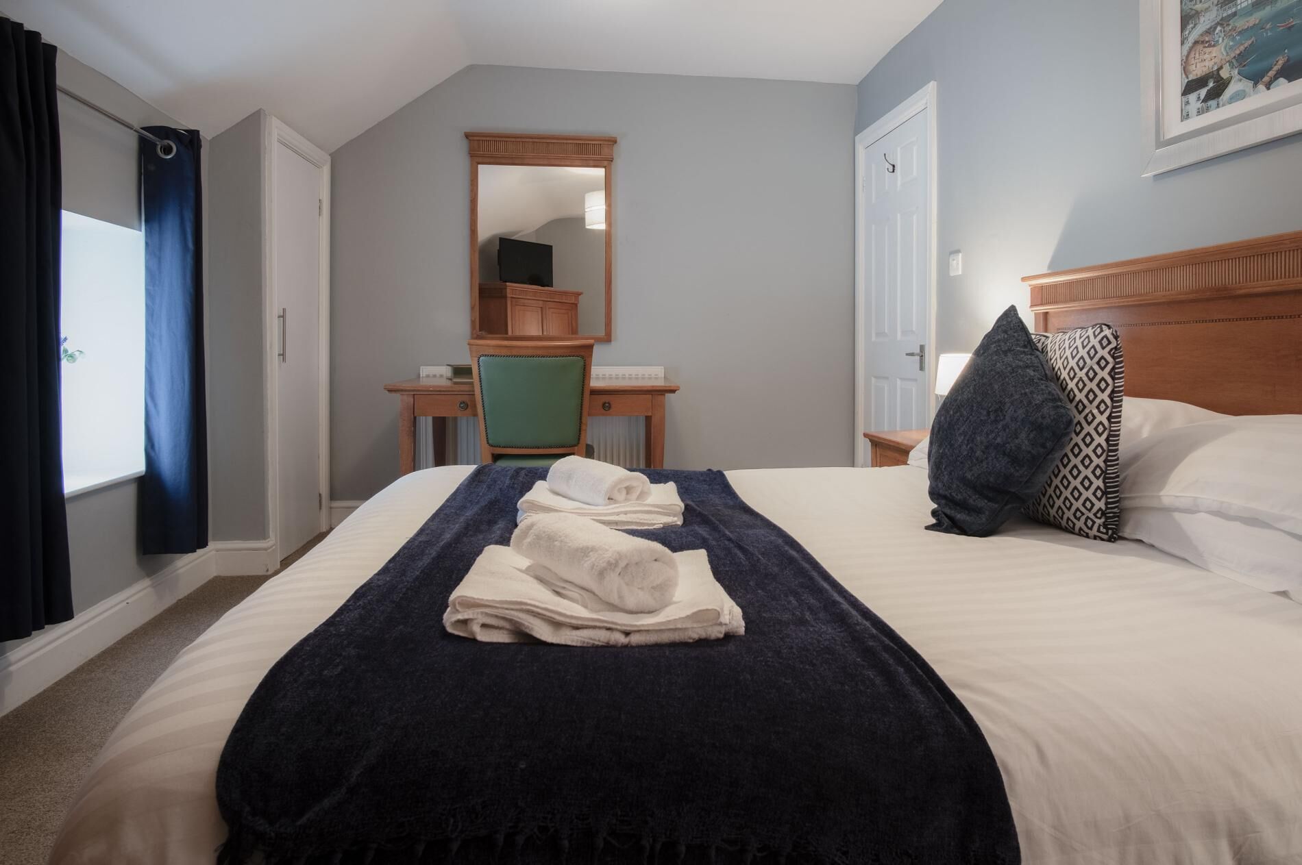 A hotel room with a large bed, a desk, a chair, and a mirror.