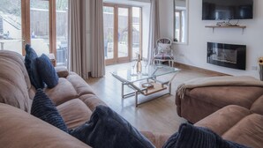A living room with a glass coffee table, beige sofas, and a TV mounted on the wall.
