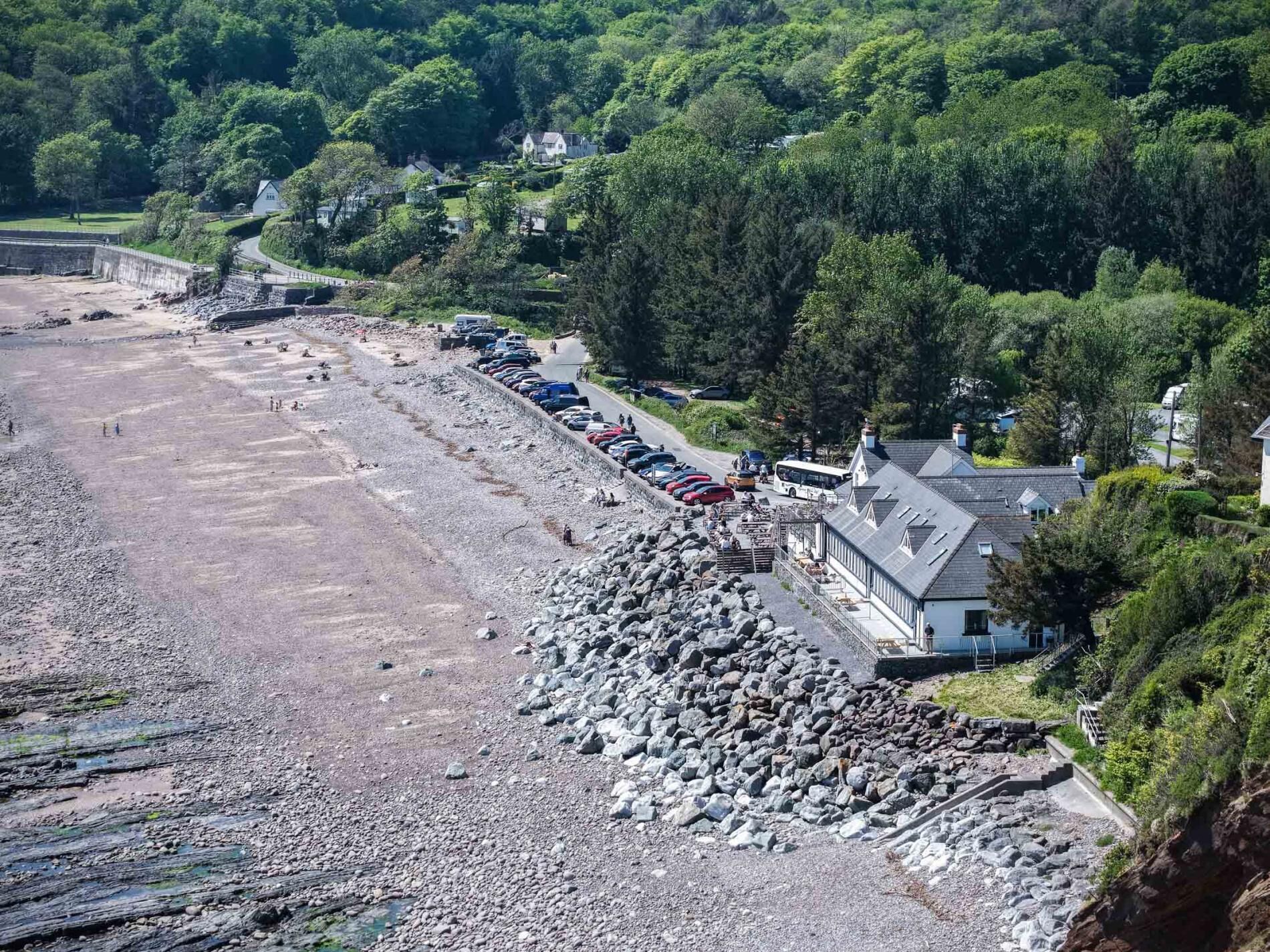 A coastal area with a rocky beach, parked cars, and a building with a sloped roof.