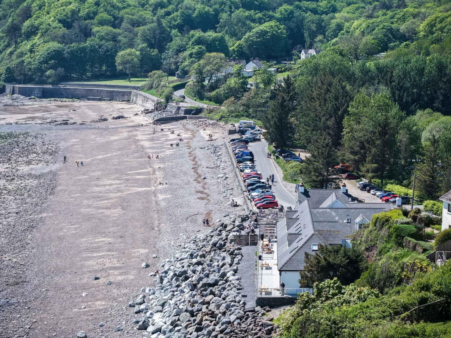 Une zone côtière comprenant un parking, une plage rocheuse et des bâtiments dotés d’un toit en pente.
