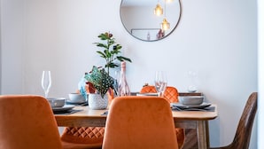 A dining area with a round mirror, orange chairs, and a table set with plates, glasses, and a plant. - No 7 Moorfield Road - 3 Bed Townhouse - Narberth (Narberth)