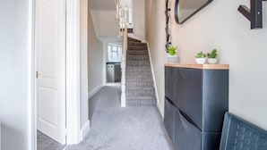A hallway with a staircase, a black cabinet with a mirror, and a plant on top. - No 7 Moorfield Road - 3 Bed Townhouse - Narberth (Narberth)