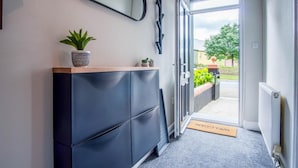 A hallway with a dark blue cabinet, a potted plant, and a welcome mat leading to an open door. - No 7 Moorfield Road - 3 Bed Townhouse - Narberth (Narberth)