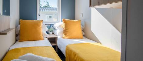 A room with two beds, each with a yellow bedspread and pillows, and a window with a view of a house.
