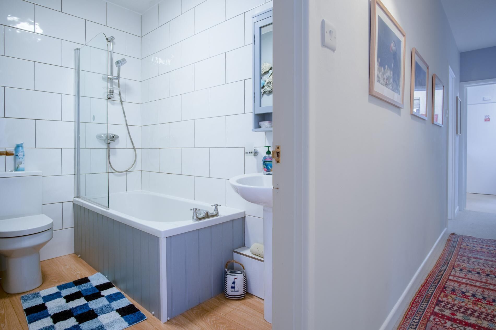 A bathroom with a bathtub, toilet, and sink, featuring white tiles and a wooden floor.