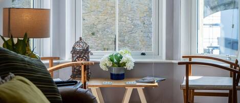 A cozy room with a wooden table, a lamp, and a view of a stone wall through a window.