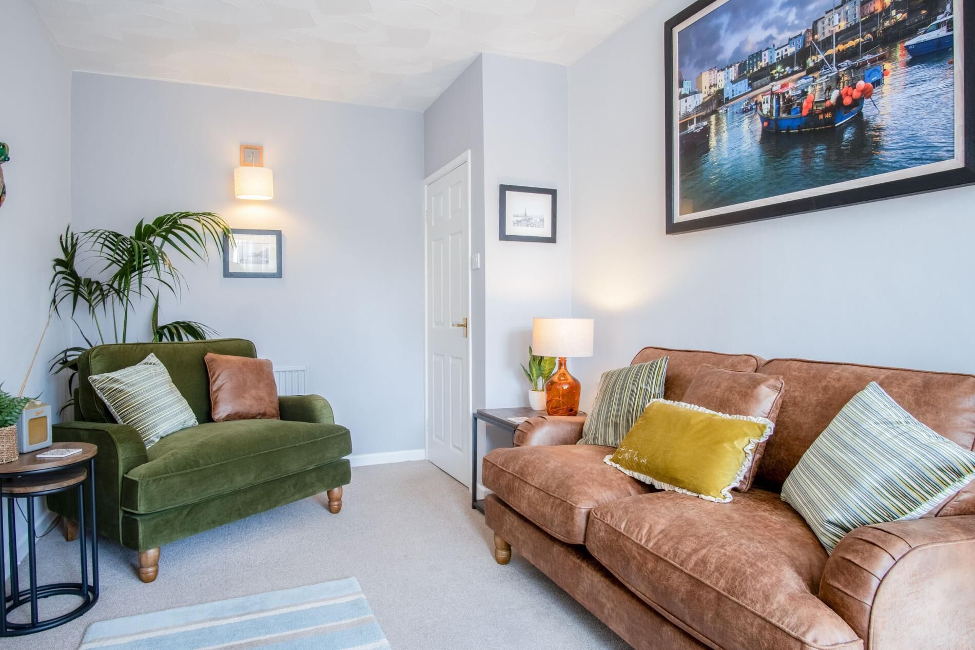 A living room with a green armchair, a brown sofa, and a framed cityscape picture on the wall.