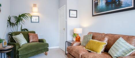 A living room with a green armchair, a brown sofa, and a framed cityscape picture on the wall.