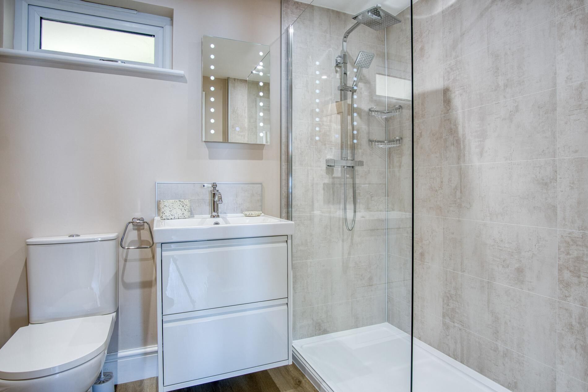 Ein Badezimmer mit Toilette, Waschbecken inklusive Spiegel und einer Duschkabine aus Glas.