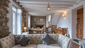 A cozy living room with a stone wall, a wooden staircase, and a dining area. - Woodcocks House - 3 Bedroom Holiday Home - Kilgetty (Kilgetty)