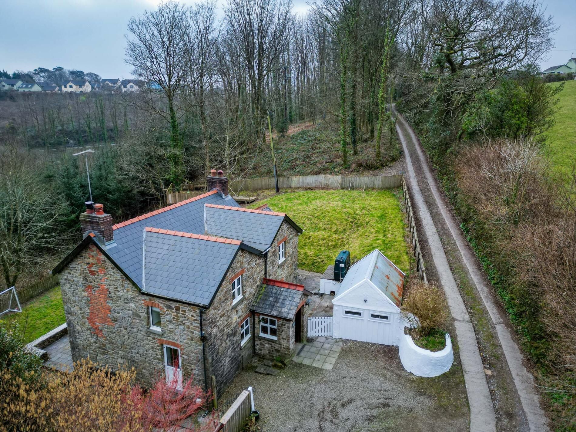 A stone house with a red roof, a white garage, and a gravel driveway.