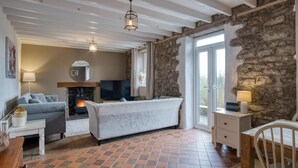 A cozy room with a fireplace, a sofa, a bed, and a stone wall. - Woodcocks House - 3 Bedroom Holiday Home - Kilgetty (Kilgetty)