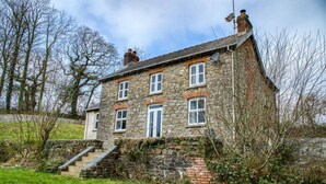 A stone house with a stone staircase leading to the entrance, surrounded by greenery. - Woodcocks House - 3 Bedroom Holiday Home - Kilgetty (Kilgetty)