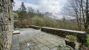 A stone patio with a stone wall and a bench. - Woodcocks House - 3 Bedroom Holiday Home - Kilgetty (Kilgetty)
