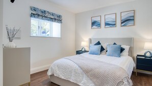 Un dormitorio con una cama grande, dos mesitas de noche, un ventanal con un adornado cortinero y tres obras de arte colgadas en la pared.
