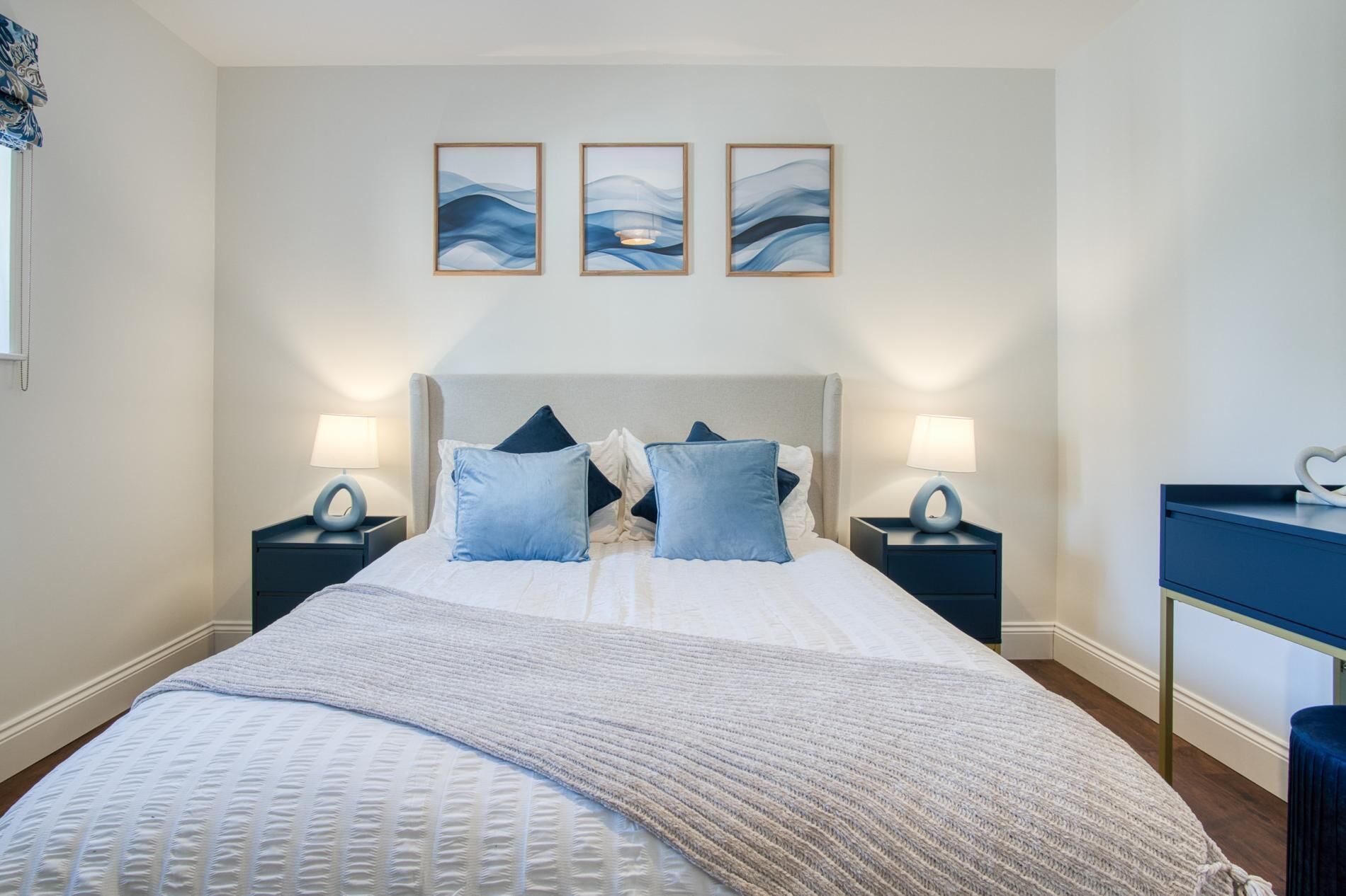 A neatly arranged bedroom with a large bed, two bedside tables with lamps, and three wall-mounted artworks.