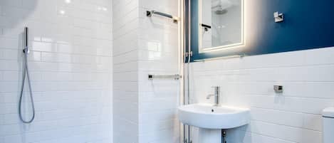 A modern bathroom with white tiled walls, a glass shower enclosure, a white sink, and a blue accent wall.