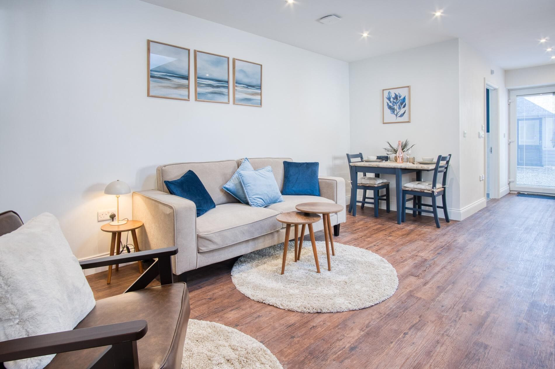 A modern living room with a sofa, two side tables, a coffee table, and a dining area with a table and chairs.