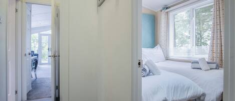 A hotel room with two beds, a desk, and a window with curtains.