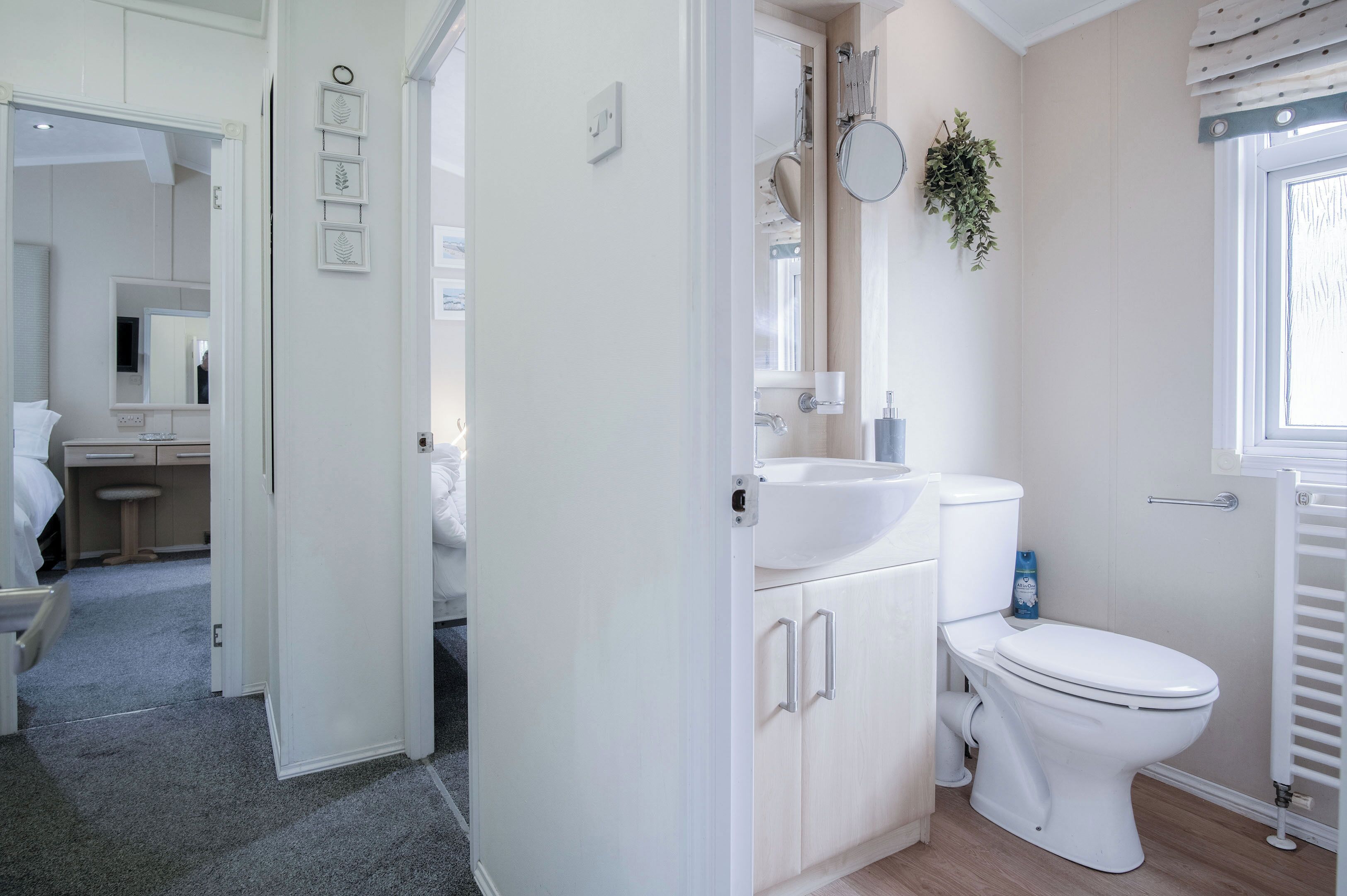A modern bathroom with a toilet, sink, and mirror. There is a window with blinds and a plant on the wall.