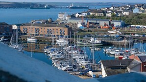 A marina with boats docked, a large industrial building, and residential houses in the background. - The Penthouse - 1 Bedroom Penthouse - Milford Haven (Milford Haven)