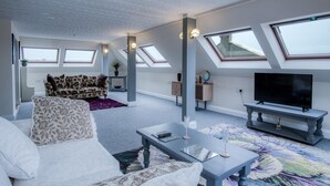 A modern living room with a sofa, a coffee table, a TV, and a patterned rug. There are skylights and a globe on a shelf. - The Penthouse - 1 Bedroom Penthouse - Milford Haven (Milford Haven)