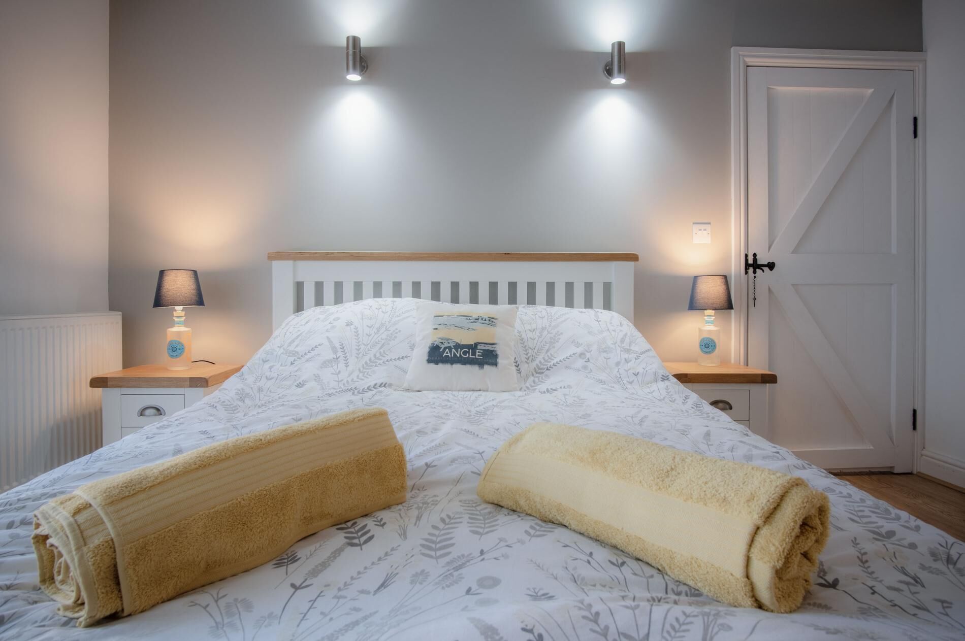Un letto rifatto con cura, coperto da una trapunta a motivi floreali, due abat-jour e una porta bianca.