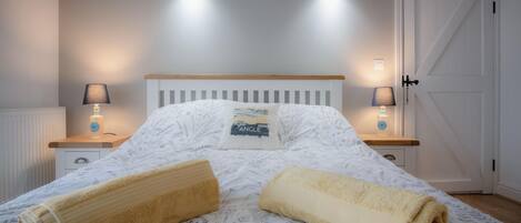 Un letto rifatto con cura, coperto da una trapunta a motivi floreali, due abat-jour e una porta bianca.