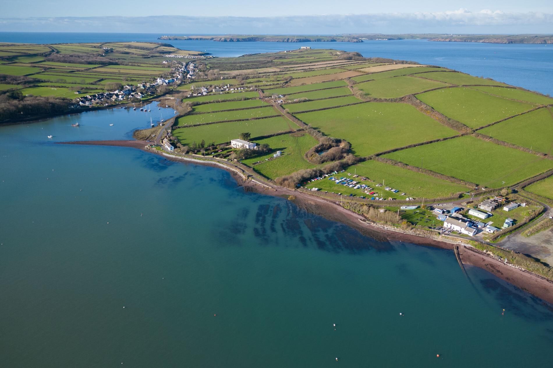 An aerial view of a coastal village with houses, fields, and a body of water.