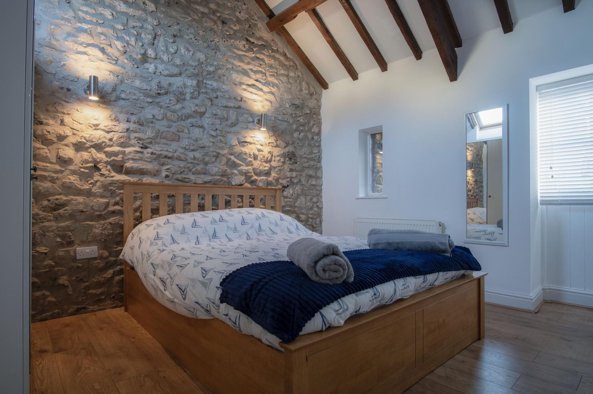 A bedroom with a stone wall, wooden bed frame, and a sloped ceiling with exposed beams.