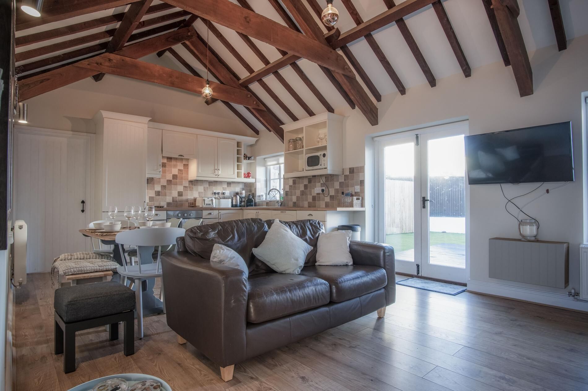 A spacious living area with a leather sofa, a dining table, and a kitchen in the background.