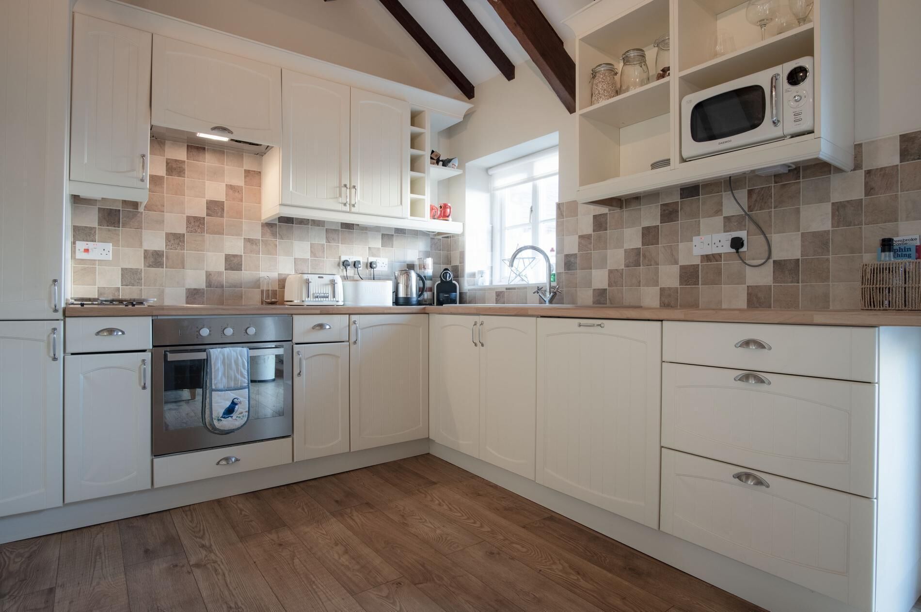 A modern kitchen with white cabinetry, a built-in oven, a microwave, and a tiled backsplash.