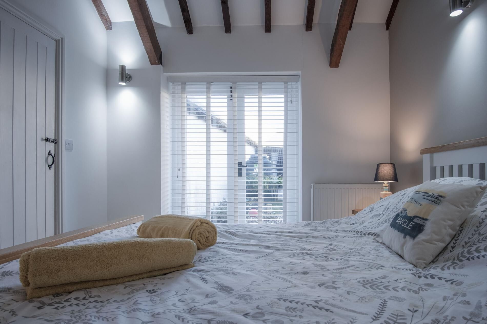 A bedroom with a bed, a window with blinds, a radiator, and a nightstand with a lamp.
