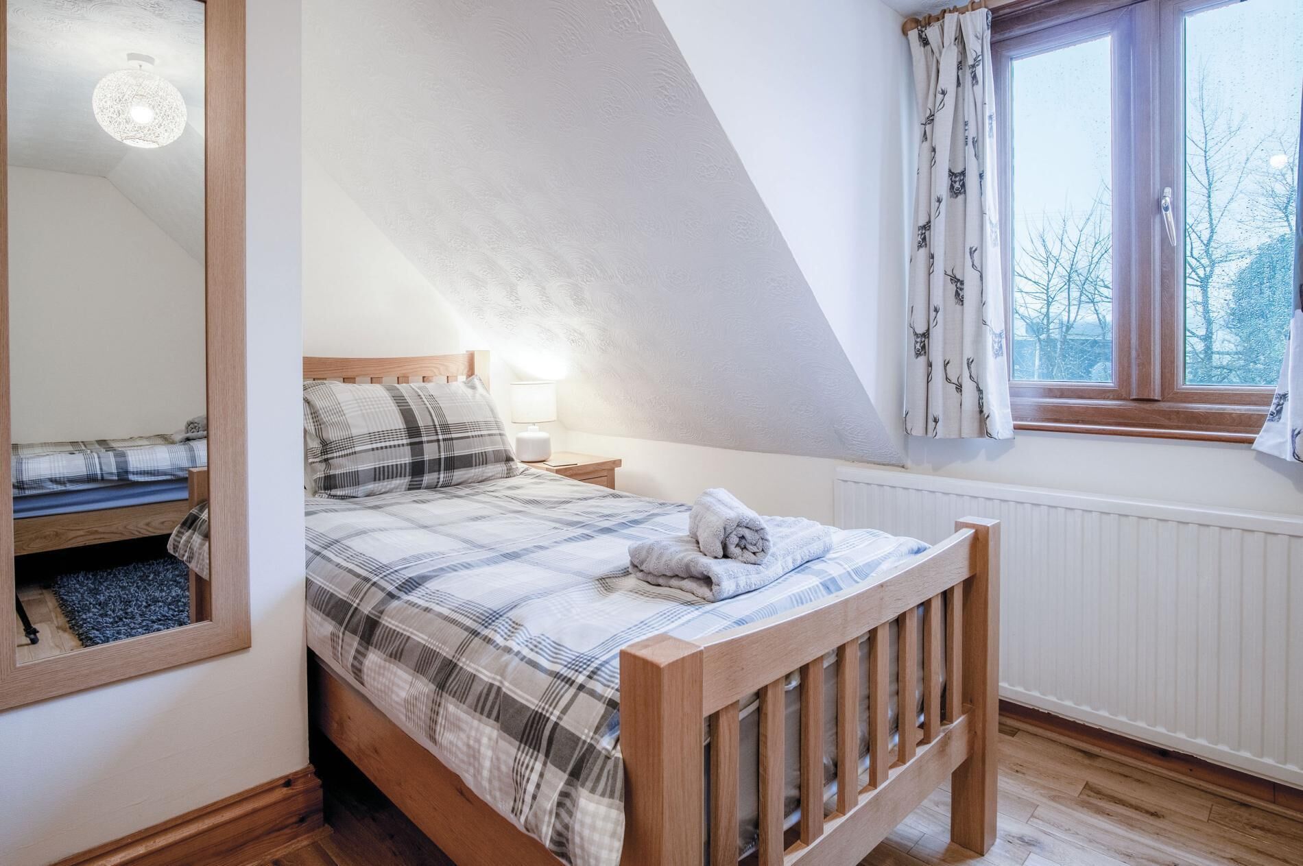 Un dormitorio con cama de madera, ventana con cortinas, radiador y espejo en la pared.