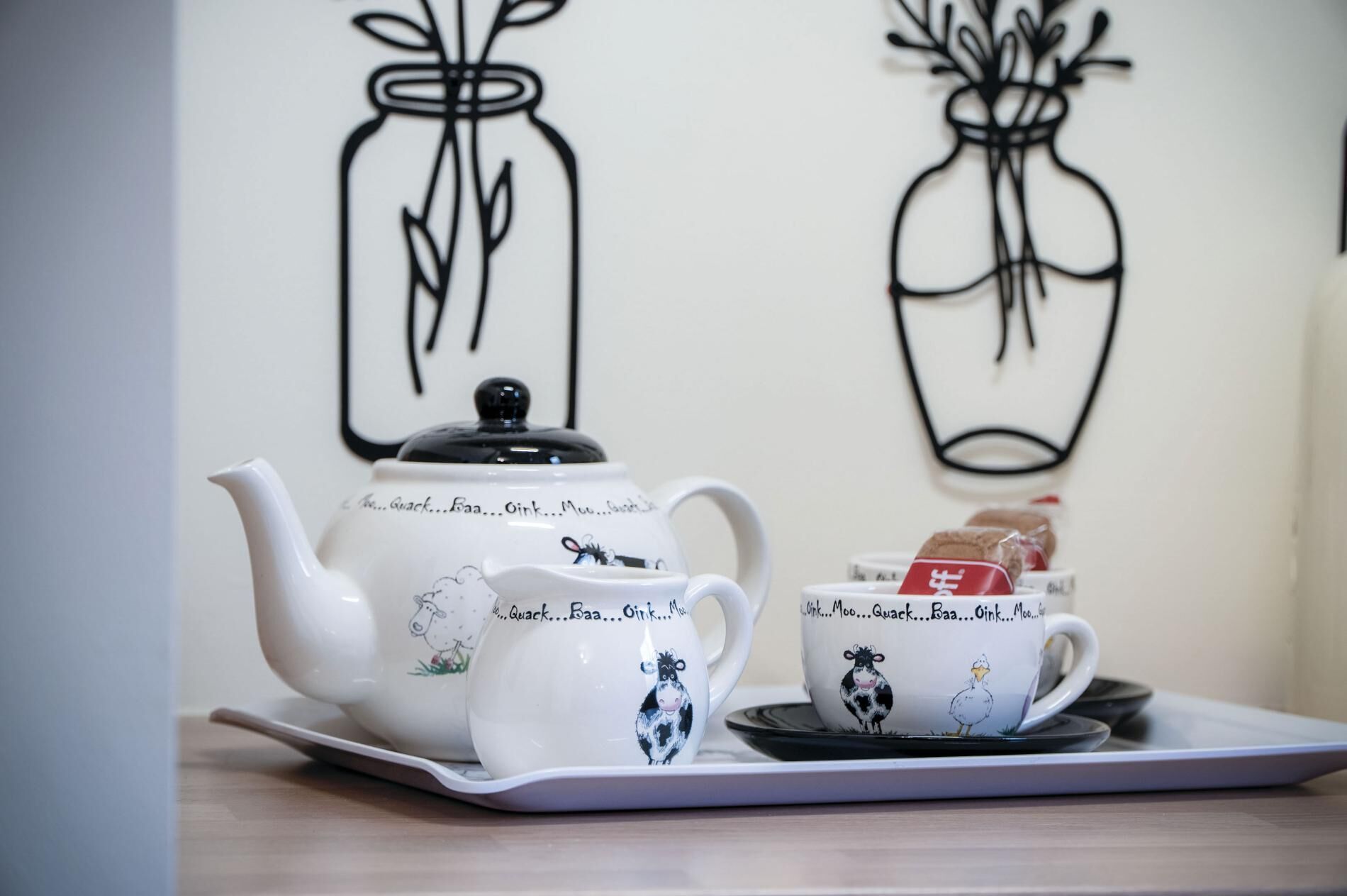 Een theeset met theepot en kopjes, versierd met een koeienprint, op een dienblad geplaatst.