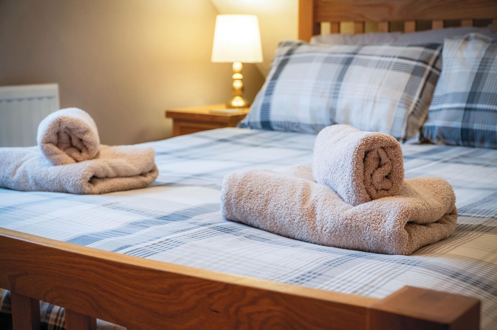 A neatly made bed with a plaid bedspread and two rolled towels on it.