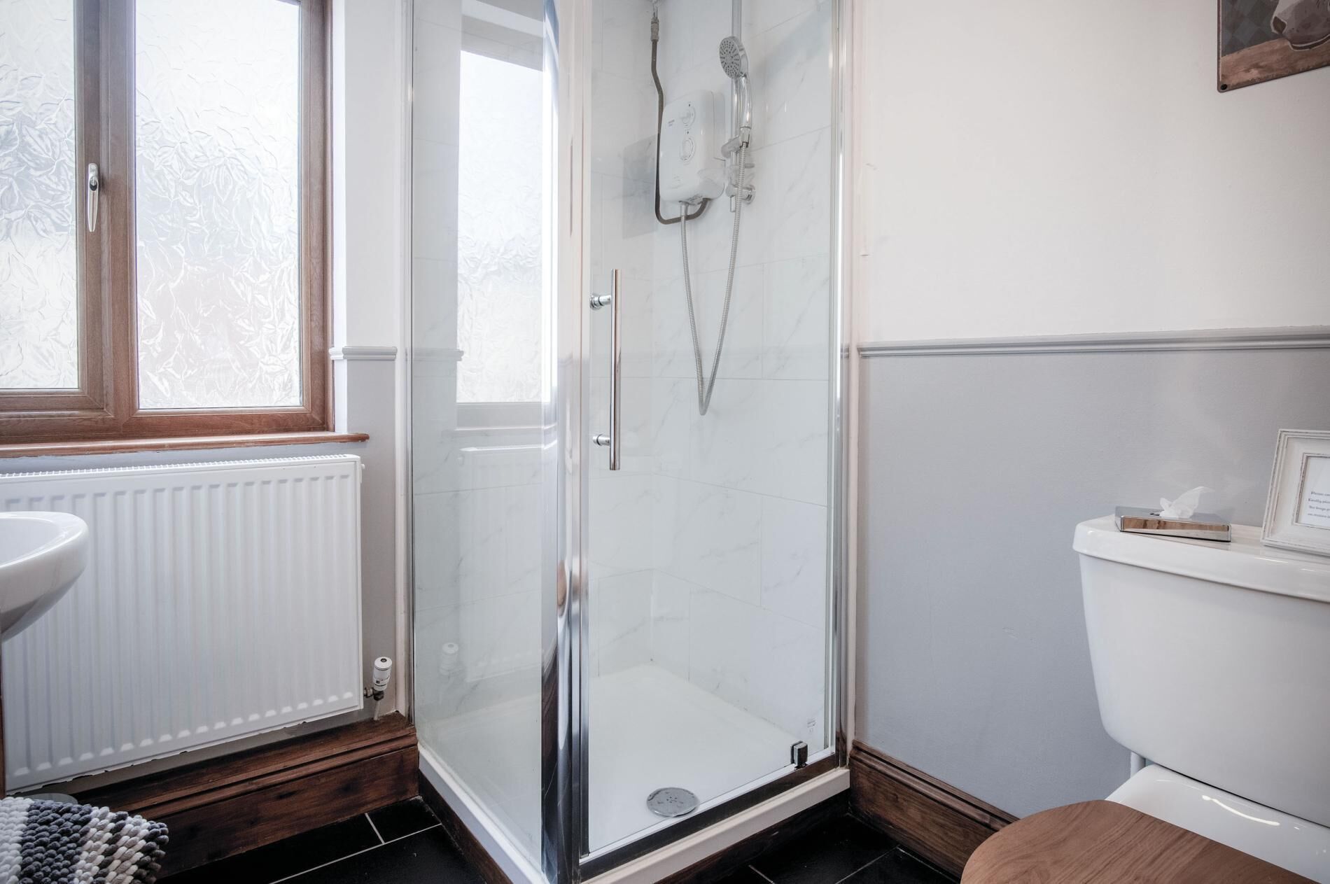 A bathroom with a glass-enclosed shower, a white toilet, and a window with frosted glass.