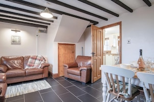 Una sala de estar acogedora con un sofá de cuero marrón, una puerta de madera y una mesa de comedor con sillas.