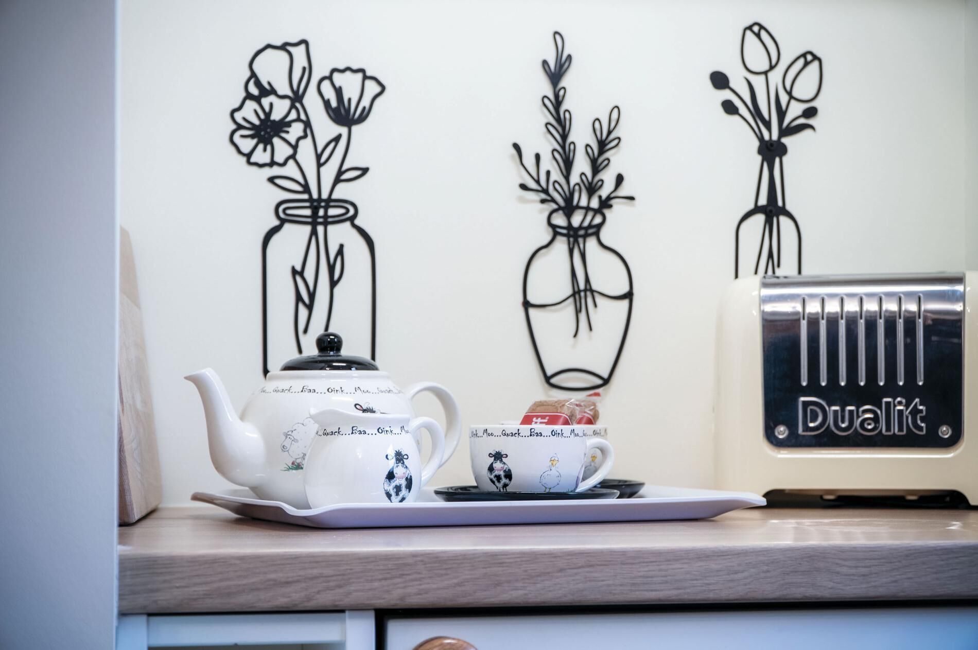 A kitchen counter with a white teapot, a cup with a cow design, and a toaster oven.