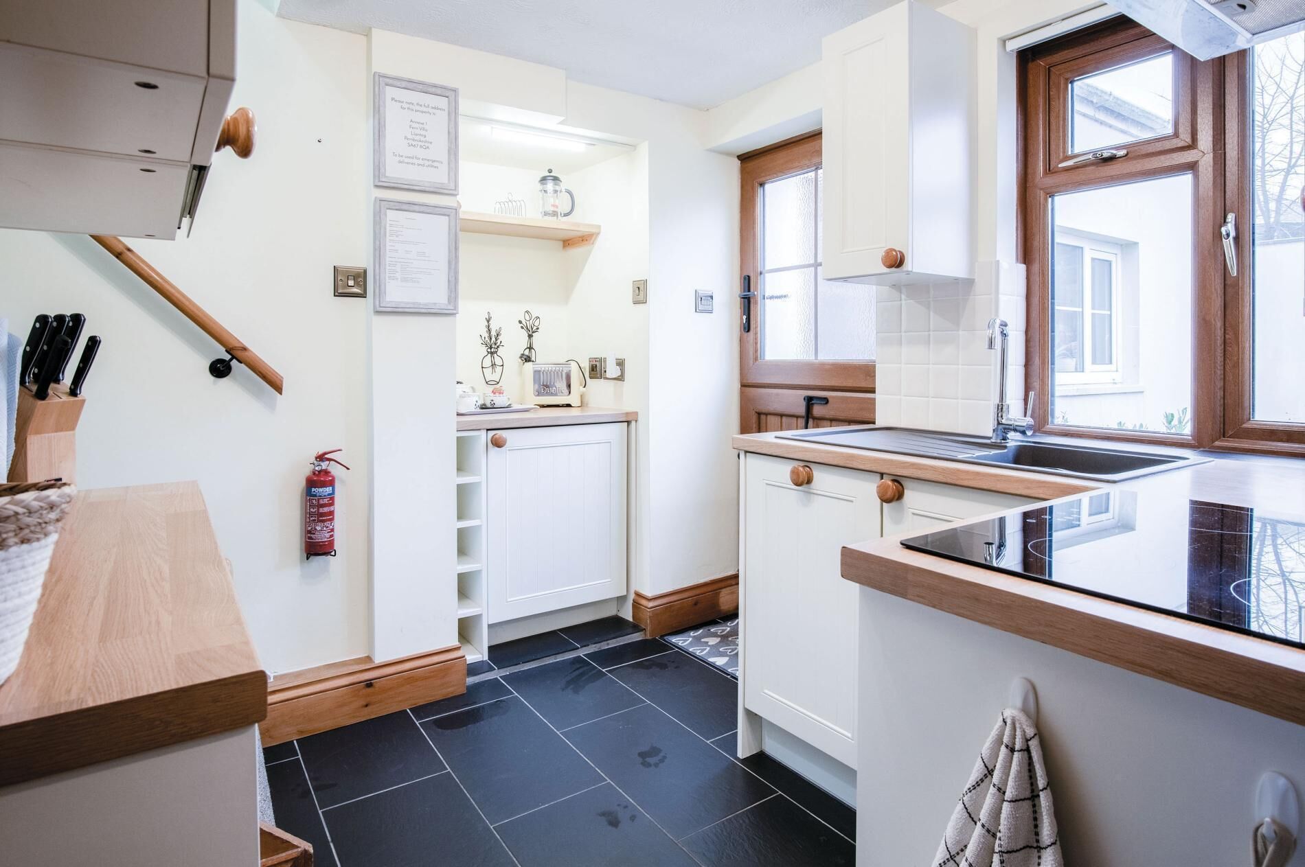 Una cocina moderna con armarios blancos, piso de baldosas negras, encimera de madera y ventana con vistas.