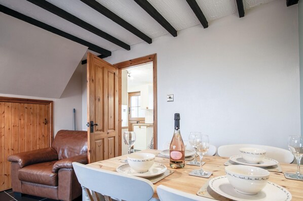 A dining area with a wooden table set for four, a bottle of wine, and matching bowls and glasses. - The Brambles - 2 Bedroom Cottage - Llanteg (Narberth)