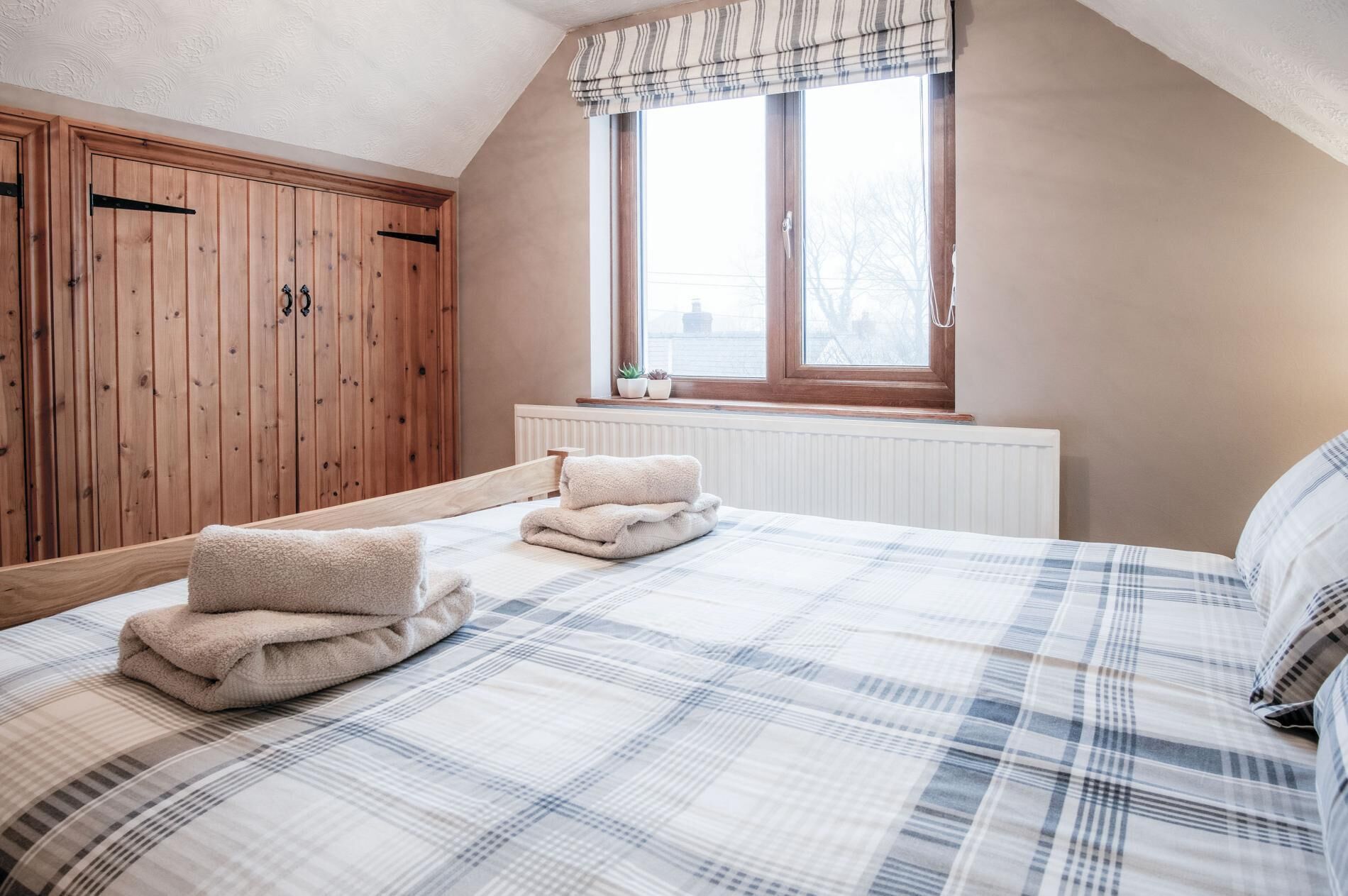 A bedroom with a bed, a window, a radiator, and wooden wardrobes.