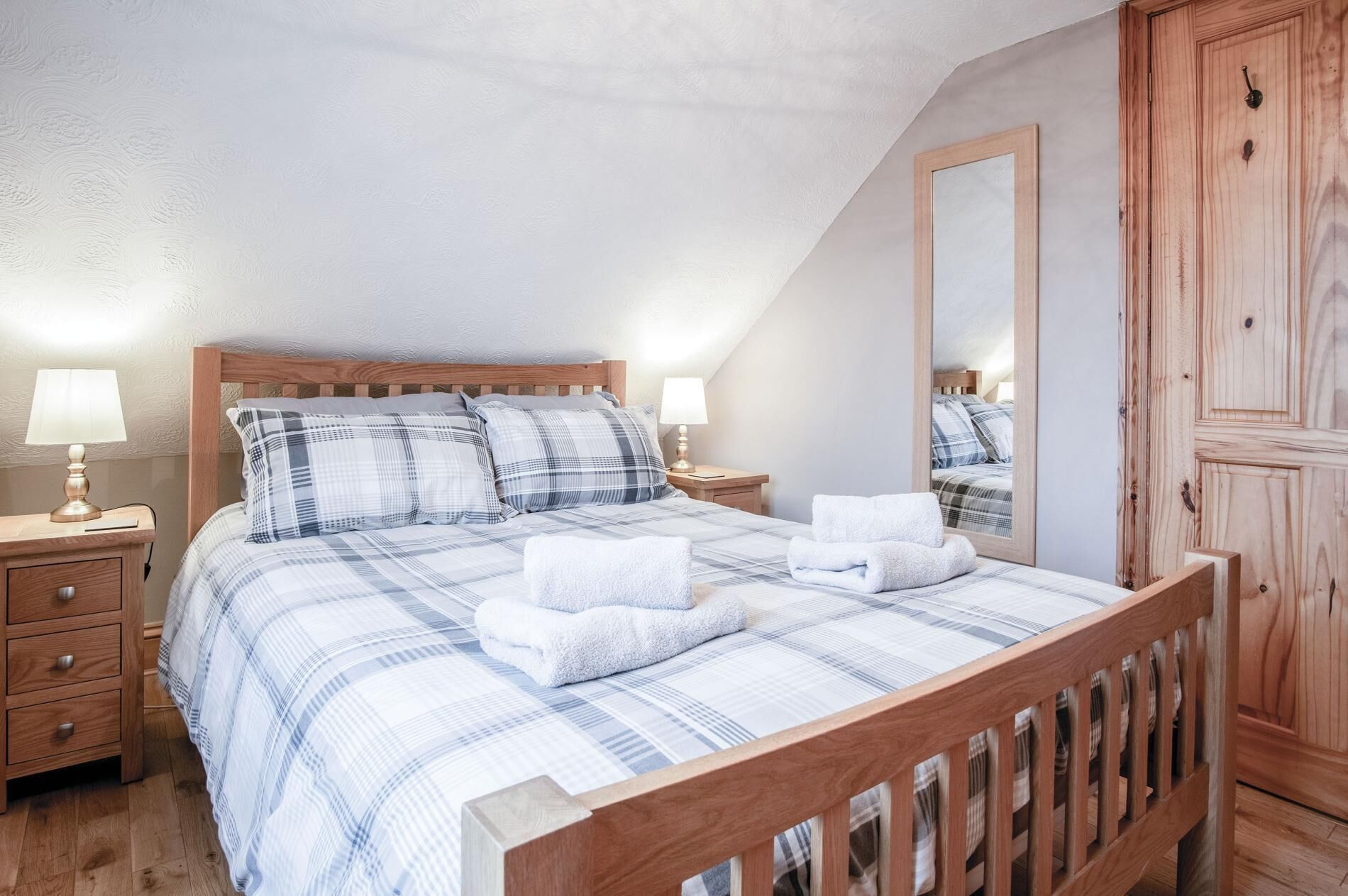 A bedroom with a wooden bed, two bedside tables with lamps, a mirror, and a wardrobe.