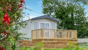 Ein Bungalow mit einer Holzterrasse und einem eingezäunten Garten.