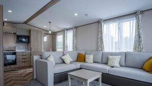 Ein modernes Wohnzimmer mit grauem Sofa, einem Couchtisch und einer Küchenzeile mit Mikrowelle und Backofen.