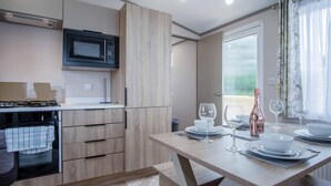 Eine moderne Küche mit integriertem Mikrowellenherd, Herd und Holzschränken. Ein Essbereich mit Tisch für zwei Personen, inklusive Weingläsern und einer Weinflasche.
