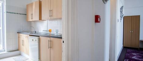 A modern kitchen with light wood cabinets, a stainless steel sink, and a red fire alarm.